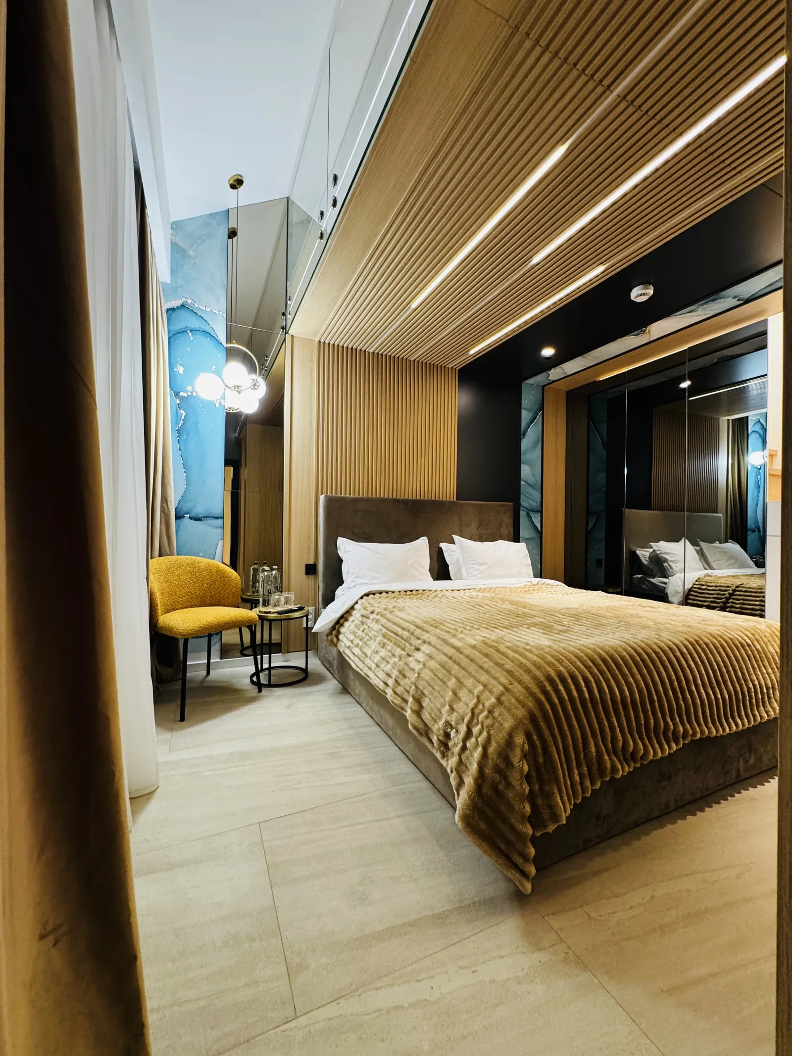 King-size bed with an upholstered armchair, a wall of blue-toned natural stone and a golden chandelier, Family Room MAPAMONT Văliug
