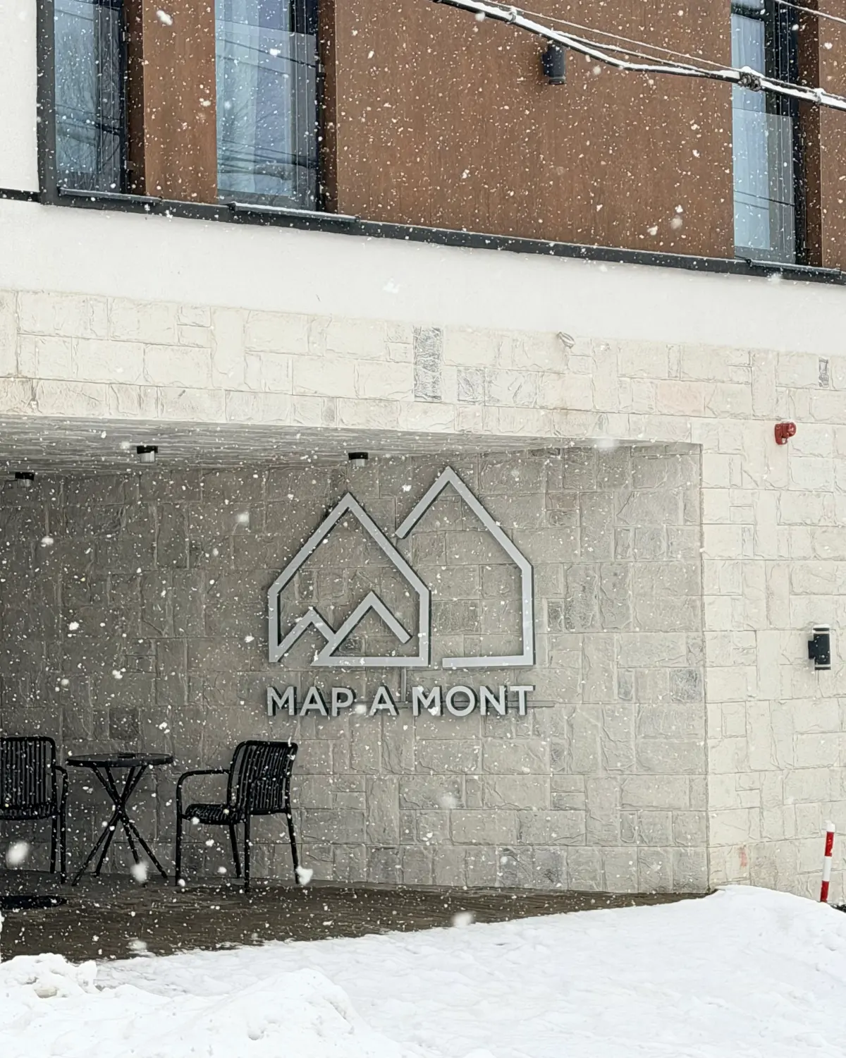 MAPAMONT guesthouse in Văliug during a snowfall, with the MAP A MONT sign on the stone wall